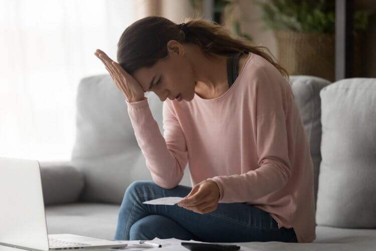 Mujer joven leyendo un papel con la mano sobre la frente preocupada