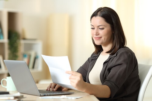 Mujer joven leyendo una carta frente a su computadora portatil