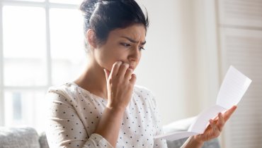 Mujer joven preocupada con la mano sobre la mejilla y viendo un documento