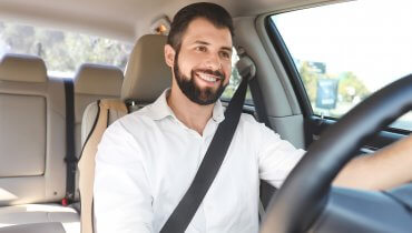 Hobre hispano con barba va manejando y sonriendo en su auto