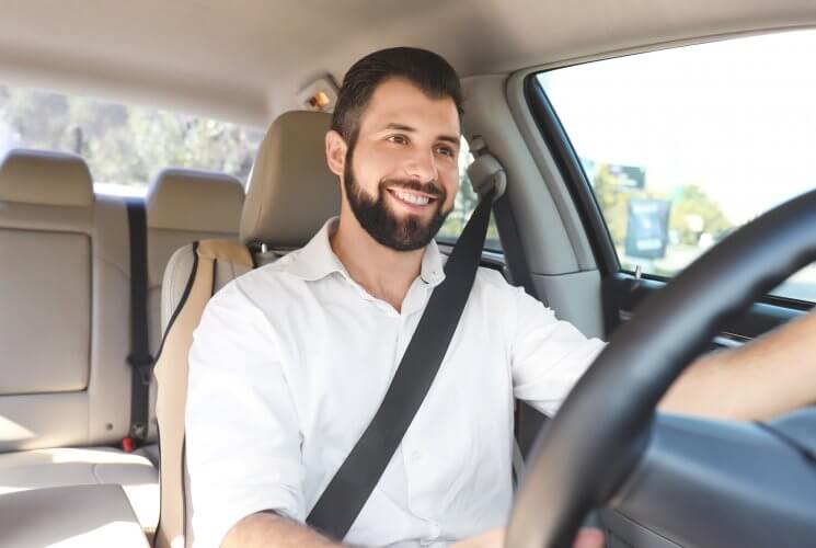 Hobre hispano con barba va manejando y sonriendo en su auto