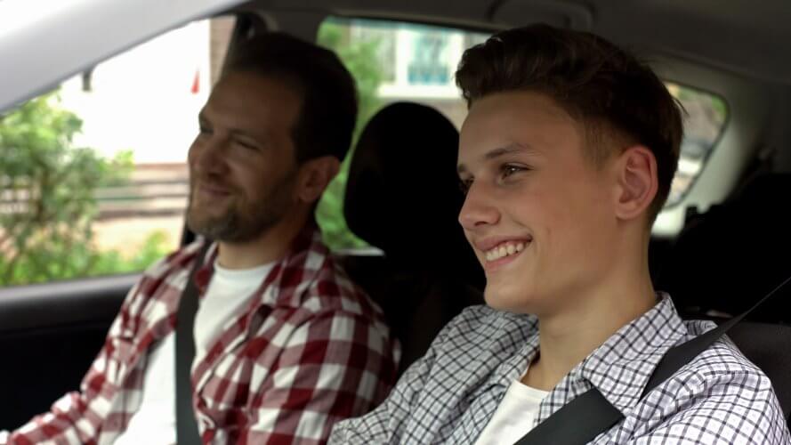 Hombre adolescente manejando con su padre a la par sonriendo