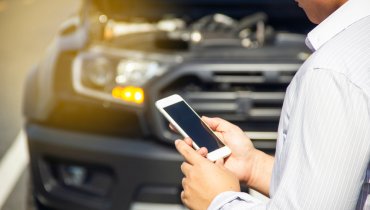 Hombre-viendo-su-celular-enfrente-de-auto-descompuesto