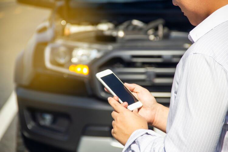Hombre-viendo-su-celular-enfrente-de-auto-descompuesto