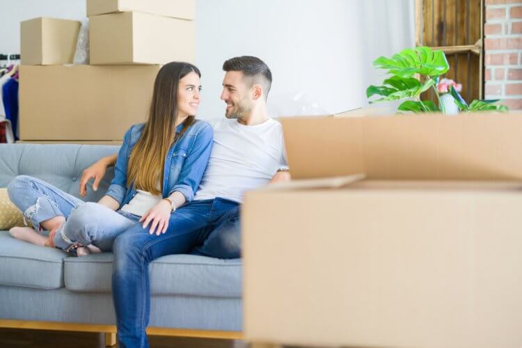 Pareja joven descansando en sillon unos momentos con cajas de mudanza a su alrededor
