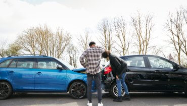 Hombre y mujer joven revisando sus autos despues de haber tenido un accidente automolivistico