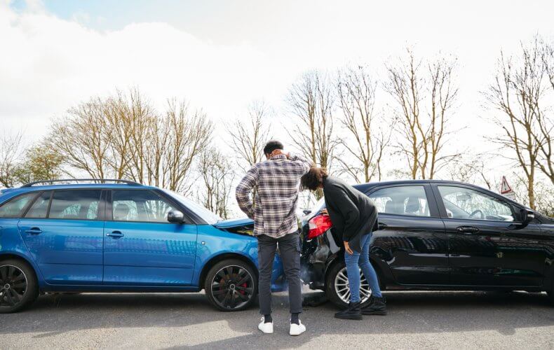 Hombre y mujer joven revisando sus autos despues de haber tenido un accidente automolivistico
