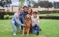 Familia hispana sonriendo en casa mientras acaricia a su perro, representando la importancia de proteger a las mascotas con un seguro en Estados Unidos.