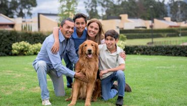 Familia hispana sonriendo en casa mientras acaricia a su perro, representando la importancia de proteger a las mascotas con un seguro en Estados Unidos.