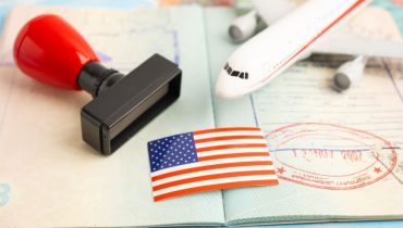 Pasaporte con sello, bandera de Estados Unidos y avión de fondo, representando los requisitos para viajar en Estados Unidos.