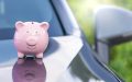 Alcancía rosa sobre el capó de un automóvil, representando ahorro o planificación financiera relacionada con gastos de auto o seguro de automóvil.
