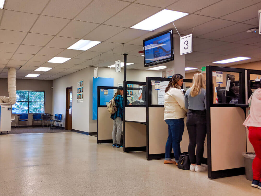 Personas esperando turno en una oficina del DMV para sacar una cita para la licencia de conducir.