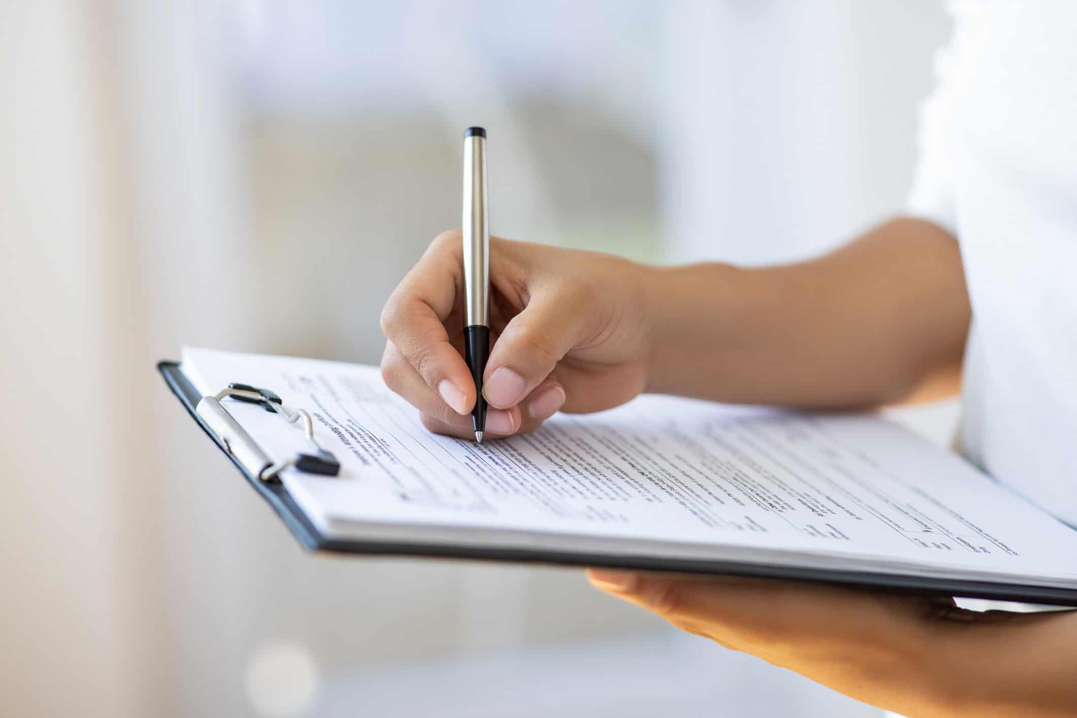 Persona completando y firmando un formulario oficial en un portapapeles, representando el proceso de registro de un carro en el DMV en Estados Unidos.