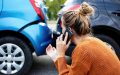 Mujer hablando por teléfono junto a dos autos con daños tras un choque, reportando el accidente y pidiendo asistencia.