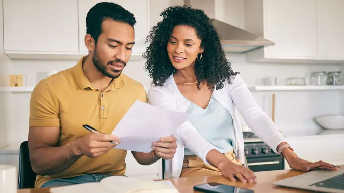 Pareja revisando documentos en la cocina mientras usan una laptop, analizando sus finanzas y organizando gastos del hogar.