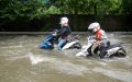 Motociclistas avanzan por una calle inundada, ilustrando cómo el seguro de moto cubre desastres naturales como inundaciones durante lluvias intensas