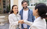 Pareja estrechando la mano de una agente frente a su nuevo hogar, representando la contratación de un seguro de inquilinos
