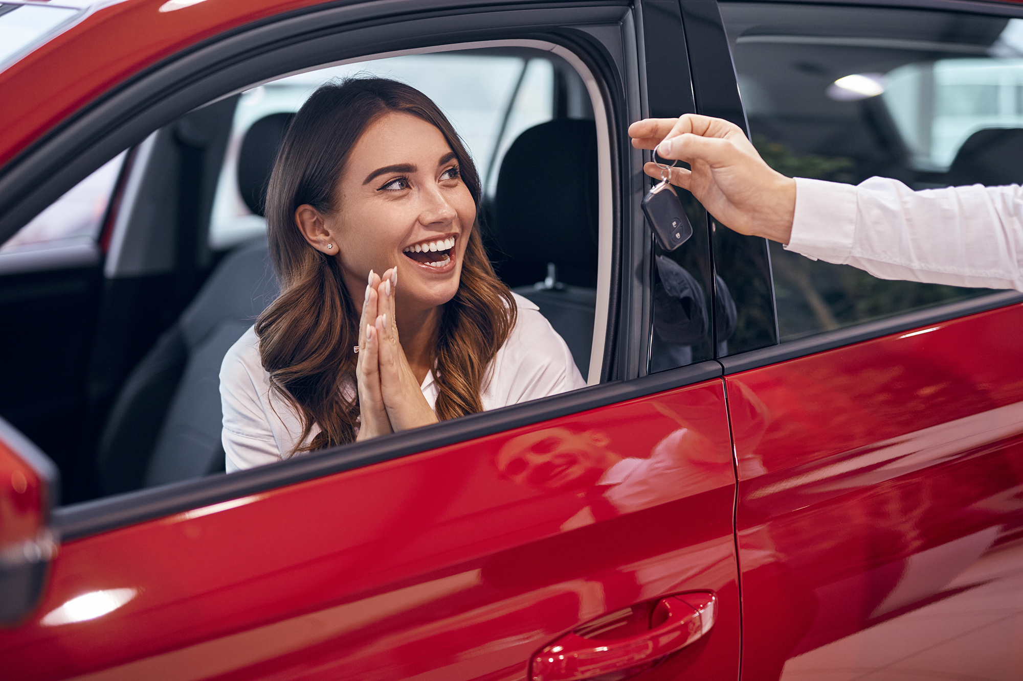 Mujer sonriente sentada dentro de un auto nuevo mientras recibe las llaves del vehículo, representando la compra y entrega de un automóvil en un concesionario.
