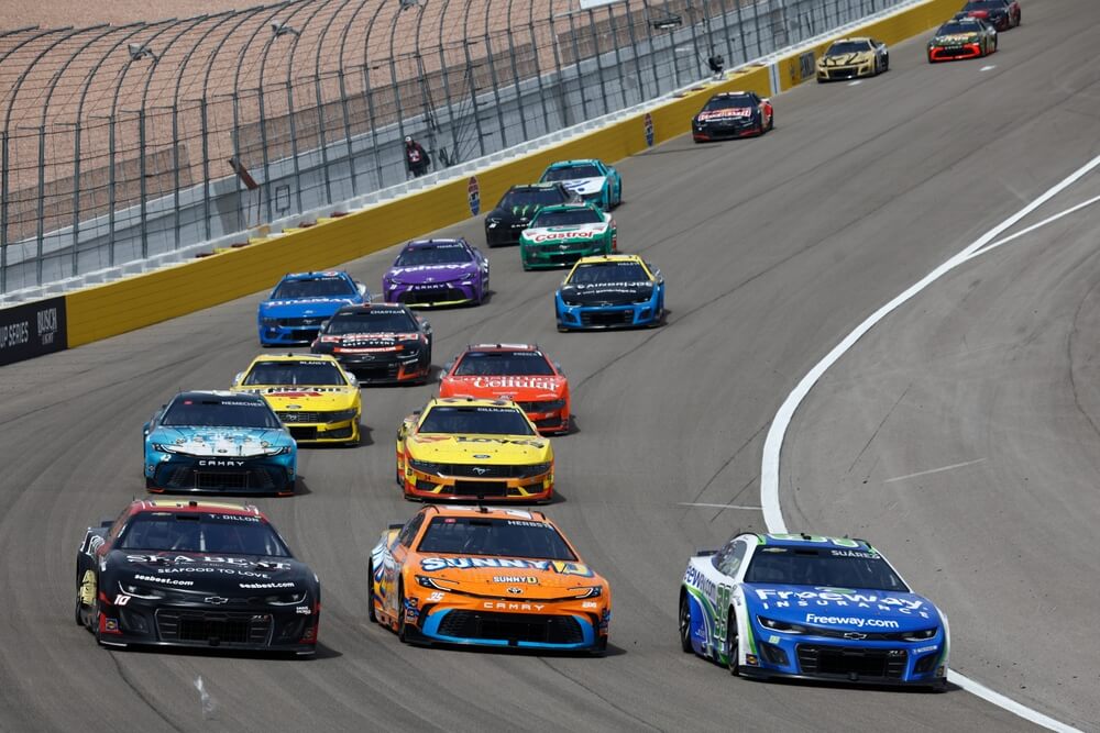 Daniel Suárez al frente del grupo en pista oval, representando a pilotos hispanos en NASCAR.