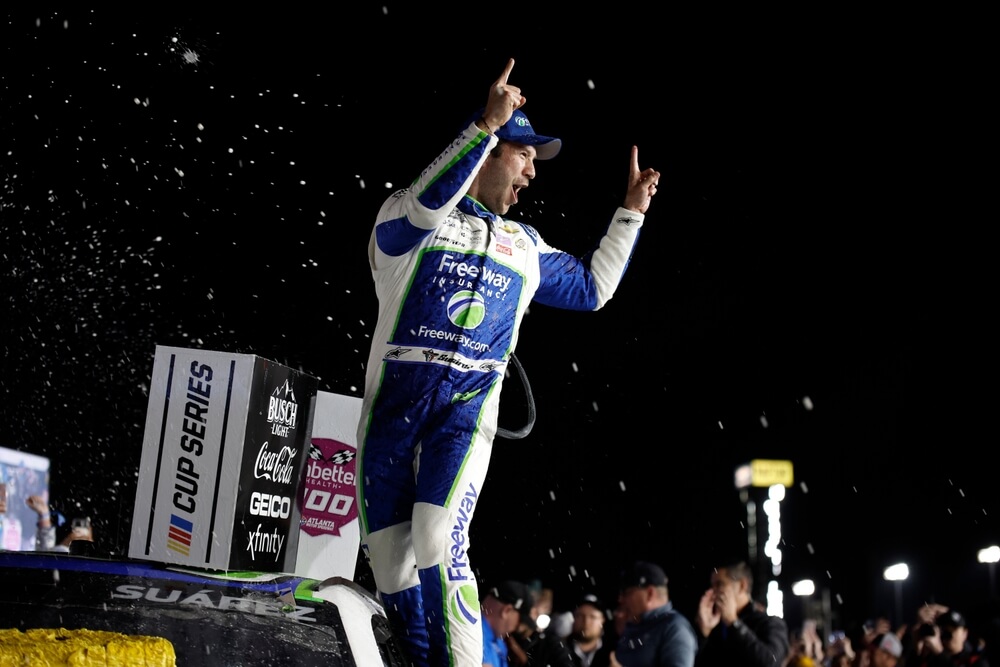 Daniel Suárez celebra la victoria sobre el auto bajo luces nocturnas, simbolizando el triunfo en las carreras de NASCAR.