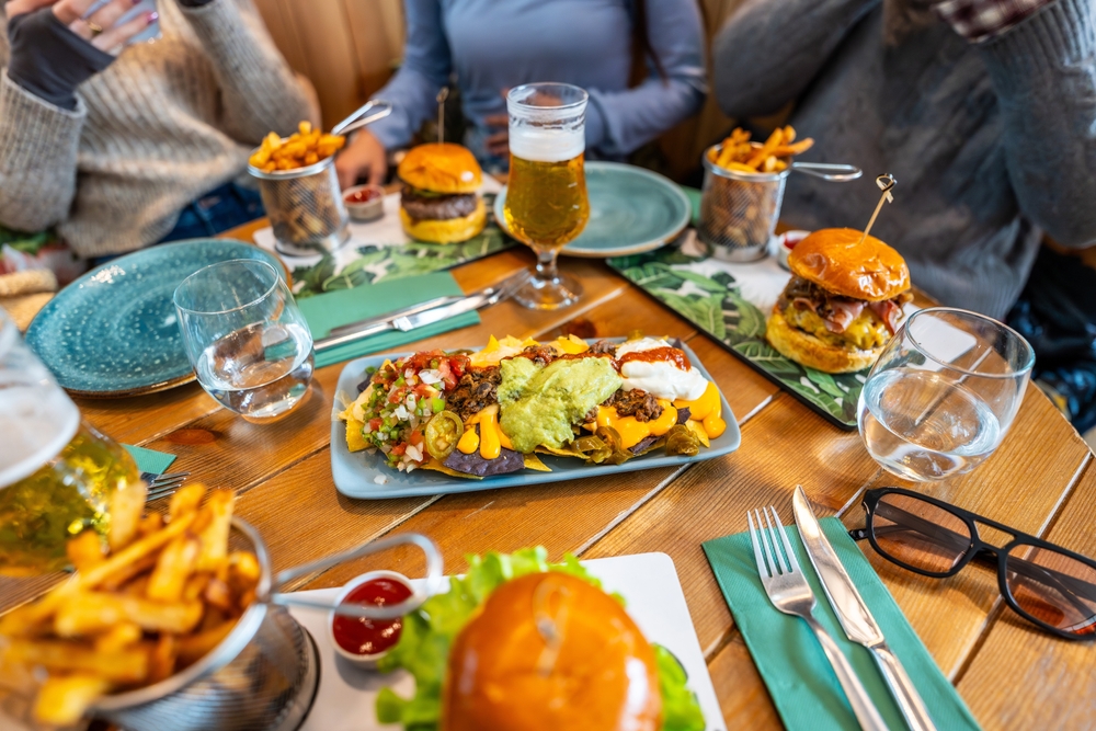 Personas compartiendo hamburguesas, nachos y papas en una mesa, representando la comida típica en NASCAR.