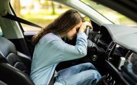 Conductora con la cabeza sobre el volante dentro del auto, ilustrando las consecuencias de manejar sin licencia
