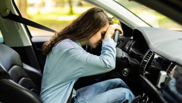 Conductora con la cabeza sobre el volante dentro del auto, ilustrando las consecuencias de manejar sin licencia