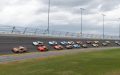 Fila de autos de carrera en pista inclinada durante competencia, mostrando la velocidad en pistas icónicas de NASCAR.