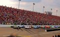 Carrera de NASCAR frente a gradas llenas de aficionados mientras los autos compiten en la pista durante un emocionante evento de automovilismo.