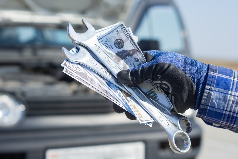 Mano sosteniendo dinero y herramientas frente a un vehículo, representando gastos ocultos de tener un auto en USA