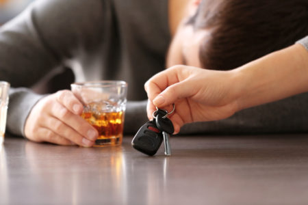 hombre ebrio sobre una mesa con una mano quitandole las llaves de su auto 