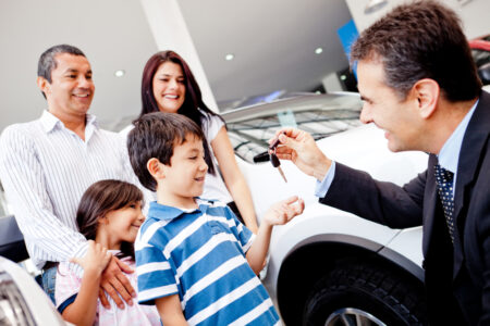 familia comprando un auto nuevo con seguro y vendendor dandole las llaves al hijo