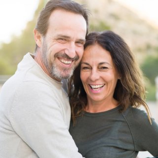 Hombre feliz abrazando a su mujer y sonriendo detrás de un paisaje verde