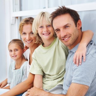 Mujer y hombre adultos abrazados junto a sus dos hijos sonrientes y felices