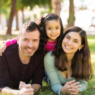 Padres de familia con su hija sonriendo recostados sobre el jardín de un parque