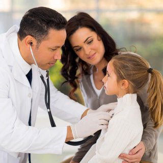 Médico joven oscultando a una pequeña niña que esta junto a su madre en el hospital