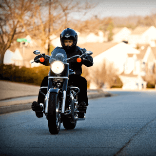 Hombre con traje negro y casco sobre una gran motocicleta negra andando en la carretera