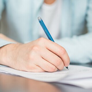 Mano de hombre sosteniendo una pluma y escribiendo sobre una hoja de papel blanco