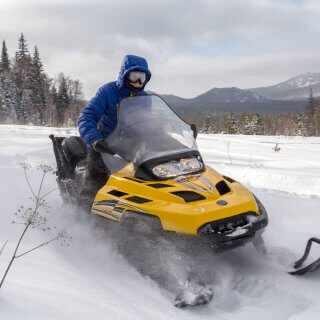 Hombre con chaqueta azul sobre motocicleta de nieve conduciendo al aire libre sobre el hielo mientras goza de seguro para motos de nieve