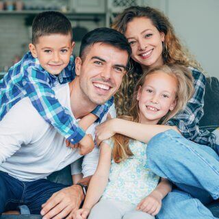 Padres de familia jóvenes abrazados junto a sus dos hijos sonrientes y felices