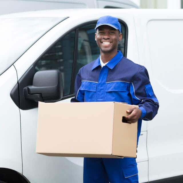 Un repartidor feliz sosteniendo una caja de cartón afuera de su carro.