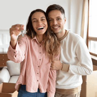 Joven pareja sosteniendo las llaves de su nuevo hogar con un seguro para casa