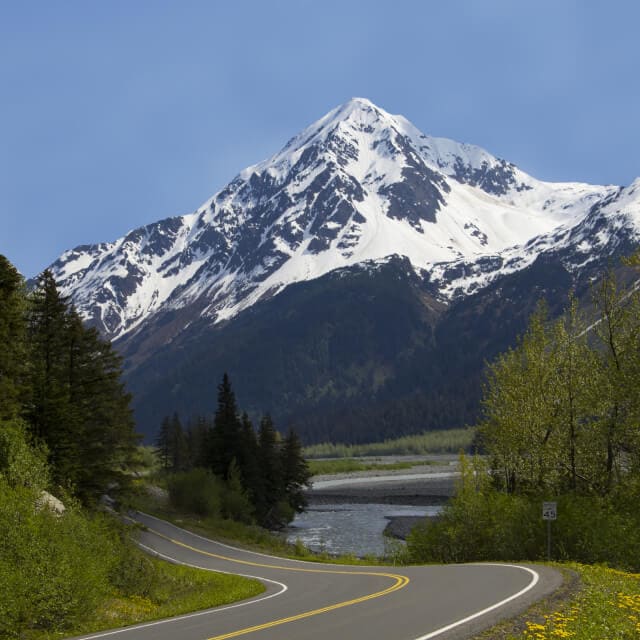 Carretera en Alaska con un paisaje de montaña nevada y bosque