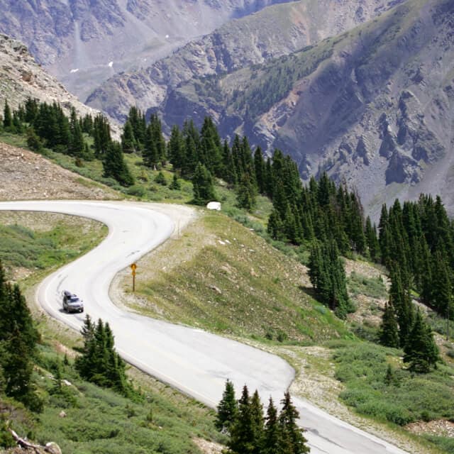 SUV en una carretera en Colorado con paisaje de árboles y montañas