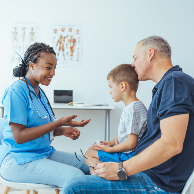 Doctor atendiendo a un niño sentado en el regazo de su padre