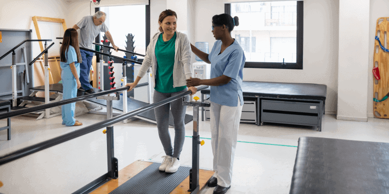 Pacientes latinoamericanos durante la fisioterapia caminando con la ayuda de barras paralelas y fisioterapeutas.