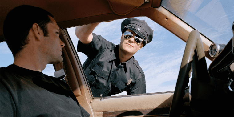 Policia deteniendo a un conductor y mirando dentro de su auto.