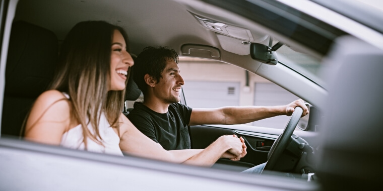 Hombre y mujer en auto manejando y sonriendo.