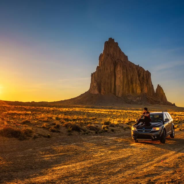Paisaje de New Mexico con una camioneta y un joven sentado en ella en una carretera solitaria.