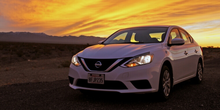 Nissan Sentra en una vía desolada con un atardecer de fondo